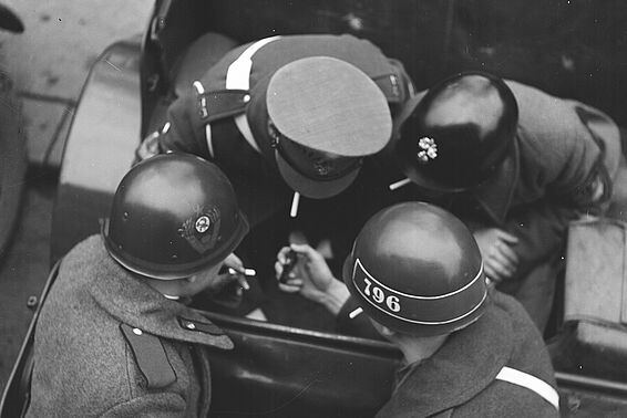 Vier Männer mit Militärhelmen oder -kappe von oben fotografiert, rauchend