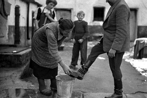 Eine Frau wäscht einem Mann die Schuhe über einem Kübel, schwarz-weiß