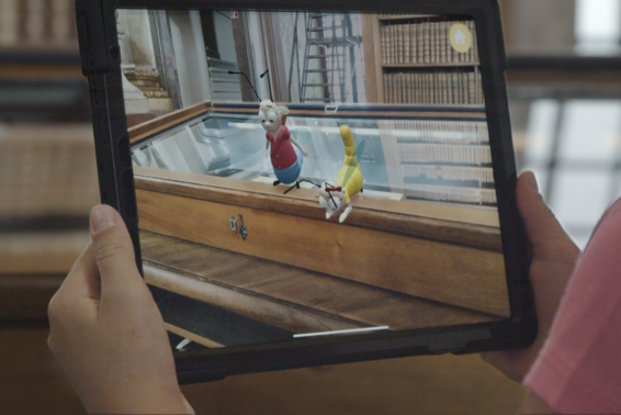 Hände halten ein Tablet mit virtuellen Bücherwürmern im Prunksaal